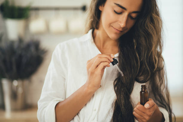 Young woman applying natural organic essential oil on hair and skin. Home spa and beauty rituals. Skin care.