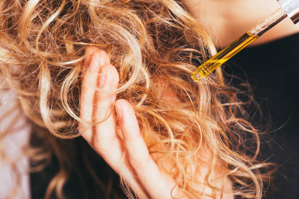 Close-up young woman applying pipette oil to her curly hair